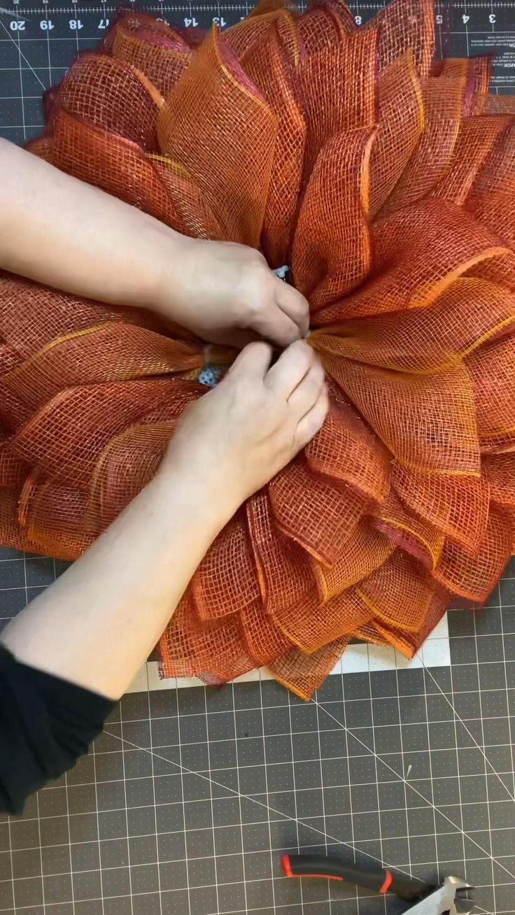 someone is working on an orange flower made out of burlocked fabric and scissors