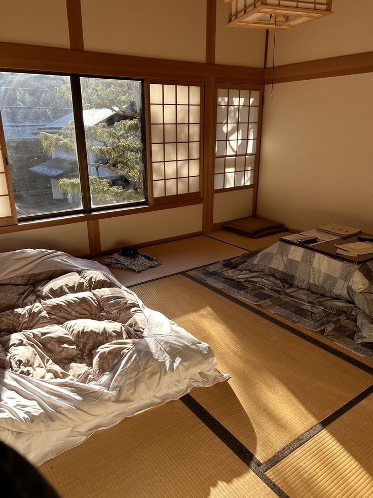 an empty room with two beds in the middle and one on the floor, next to a large window