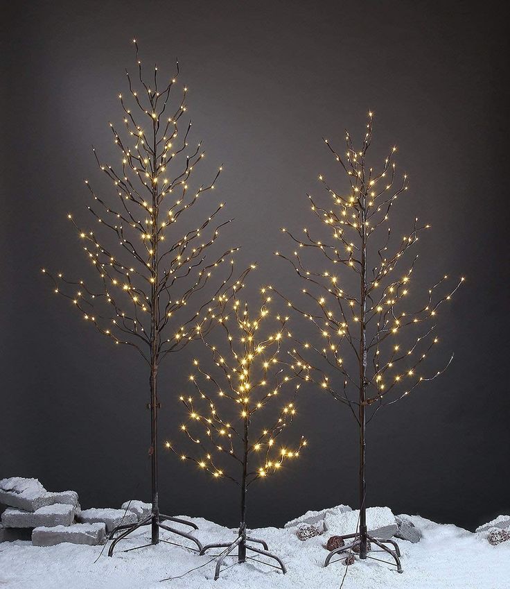 three small trees with lights on them in the snow