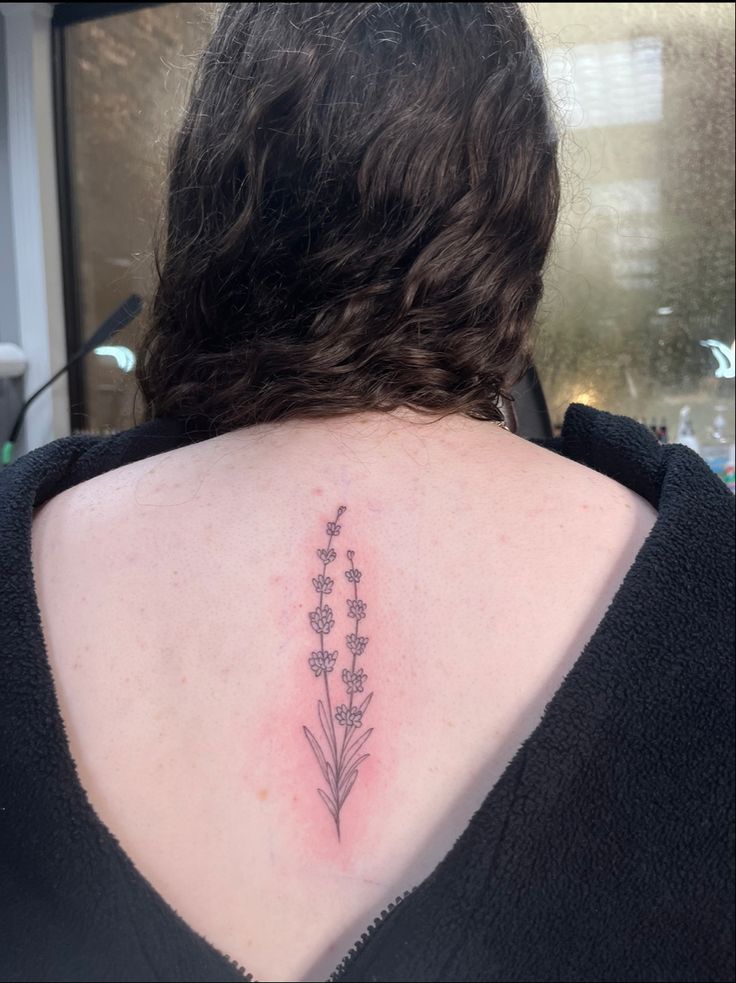 the back of a woman's neck with small flowers on her left shoulder and lower back