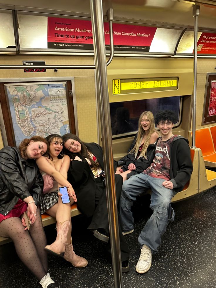 four people are sitting on a subway car together and posing for the camera with their arms around each other