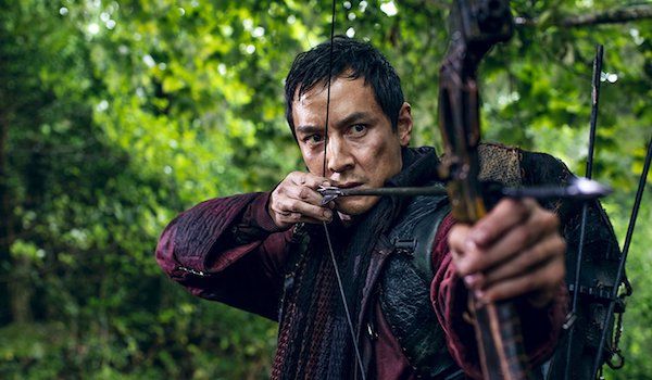 a man holding a bow and arrow in his hand while looking at the camera with an intense look on his face