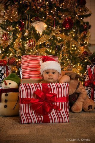 a baby wearing a santa hat and sitting in front of a christmas tree with presents