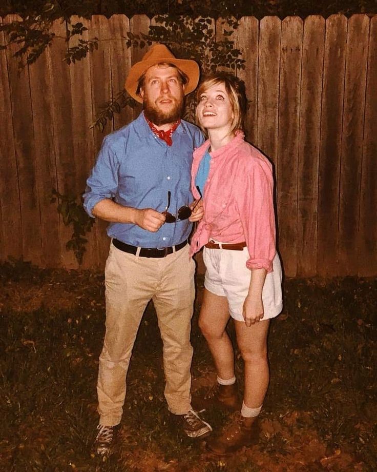 a man and woman standing next to each other in front of a wooden fence at night