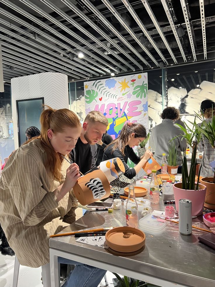 a group of people sitting around a table working on crafting projects with plants in the background