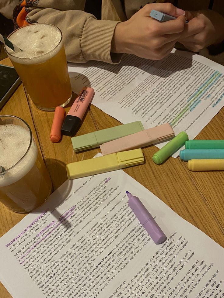 two people sitting at a table with papers and pens in front of them, one holding a cell phone