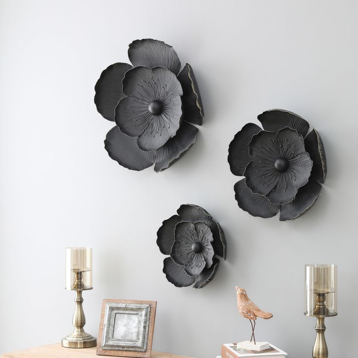 three metal flowers are mounted on the wall above a small table with candles and pictures