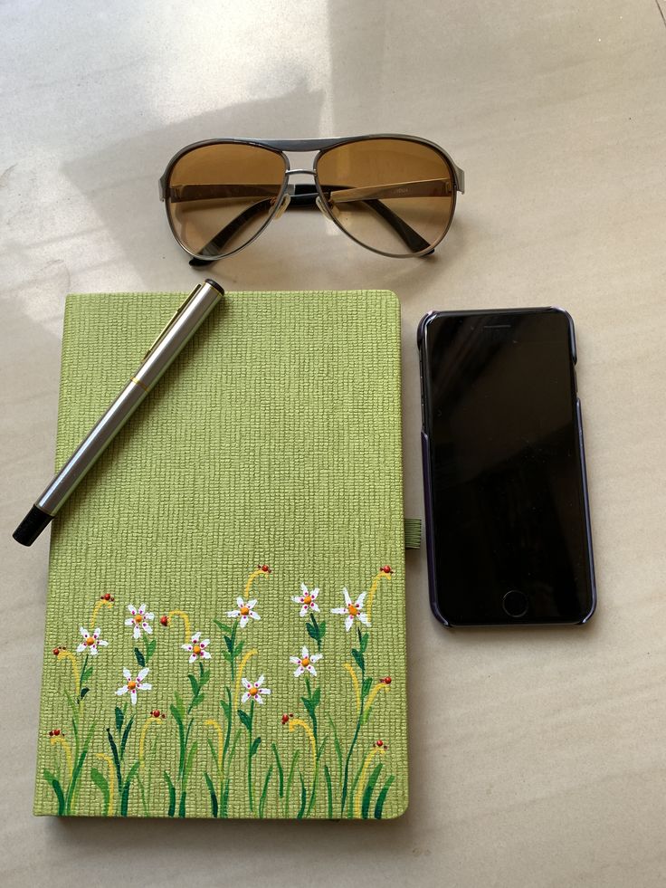 a cell phone and sunglasses on a table next to a notebook with an embroidered cover