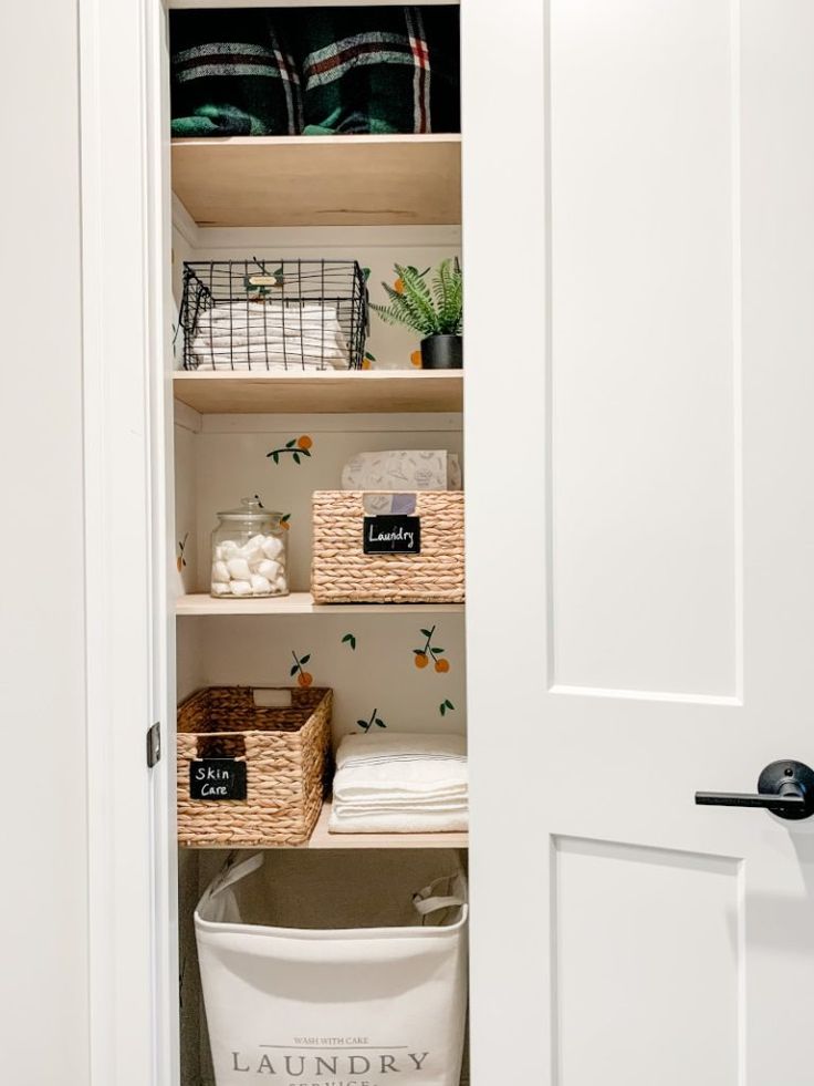 an open closet with baskets and laundry items on the bottom shelf, next to a white door