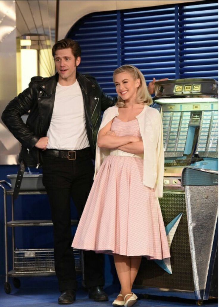 a man and woman standing next to each other in front of a blue wall with shutters