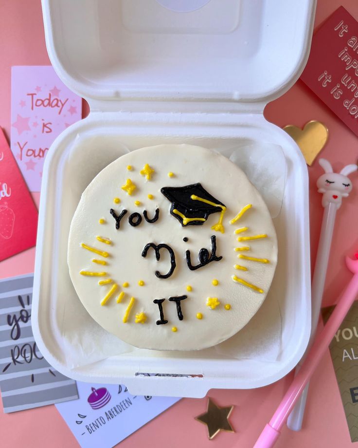 a decorated cake in a white box with writing on it and graduation decorations around the edges