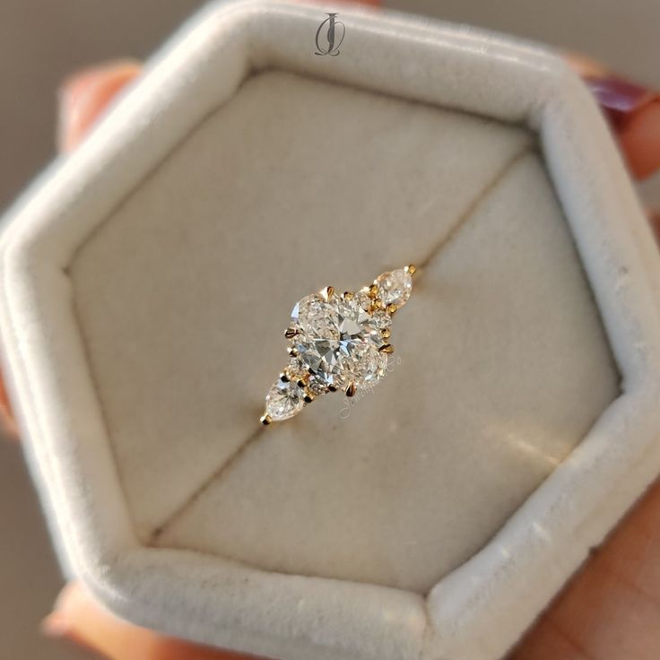 a close up of a person's hand holding an engagement ring in a box