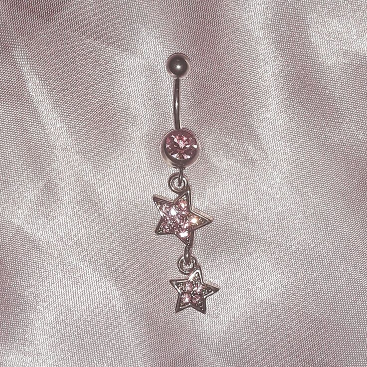 a pair of stars dangling from a navel bar on a shiny silver fabric background