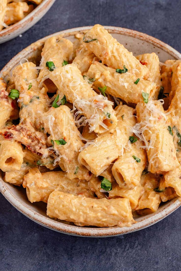 two bowls filled with pasta and parmesan cheese on top of a blue table