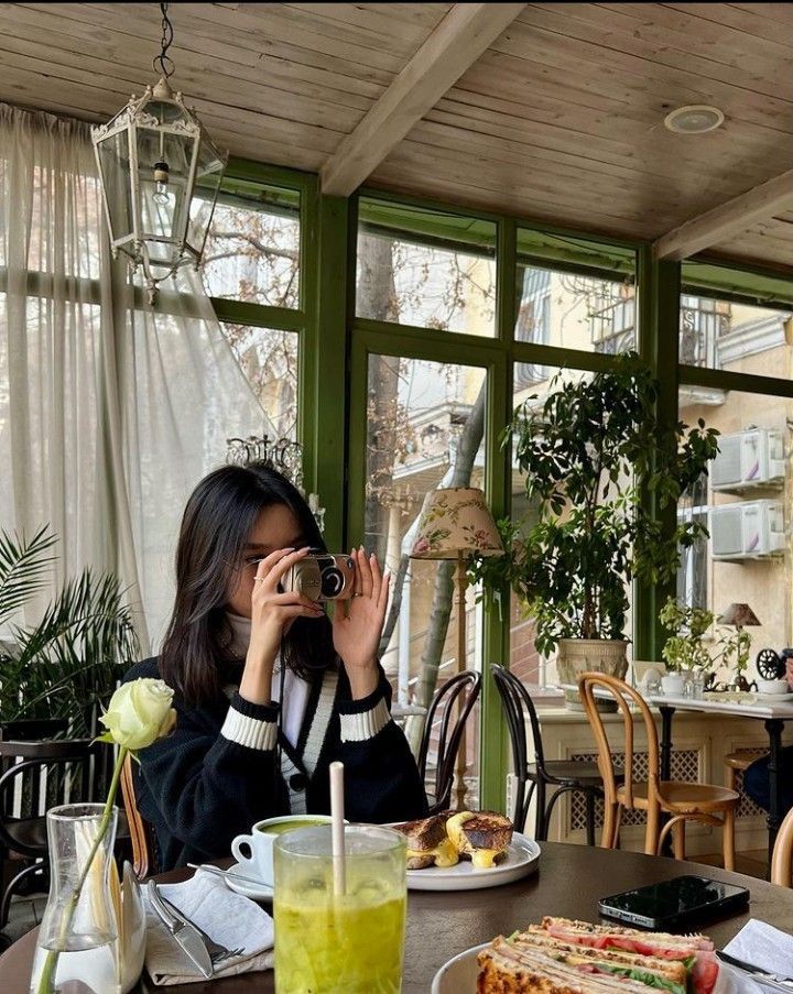 a woman sitting at a table with food and drinks in front of her taking a photo