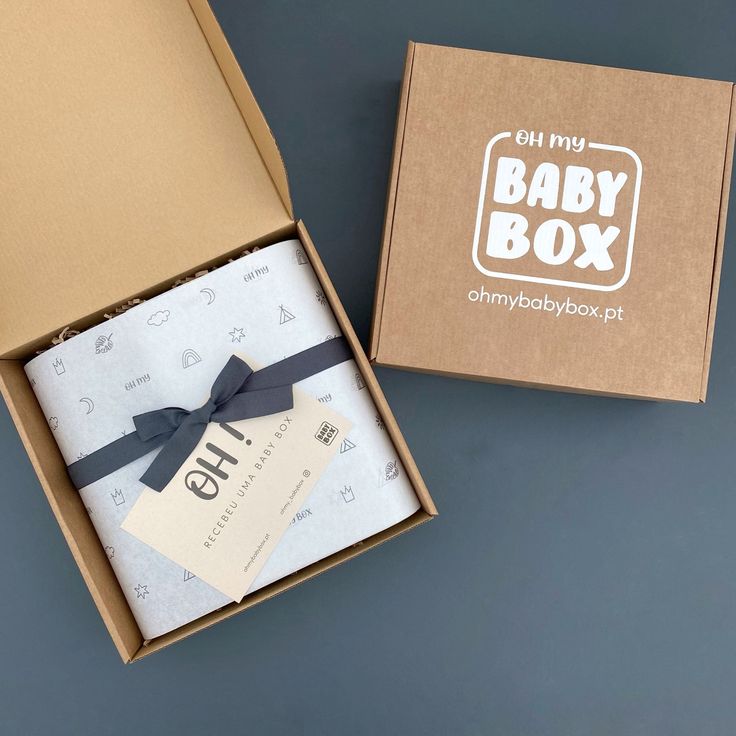 an open box with a baby blanket inside it and a tag on the lid that says oh my baby box