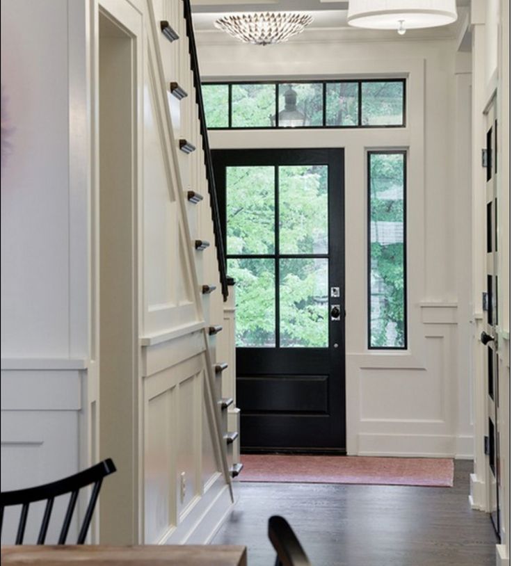 a staircase leading to a black door and window in a white house with wood flooring