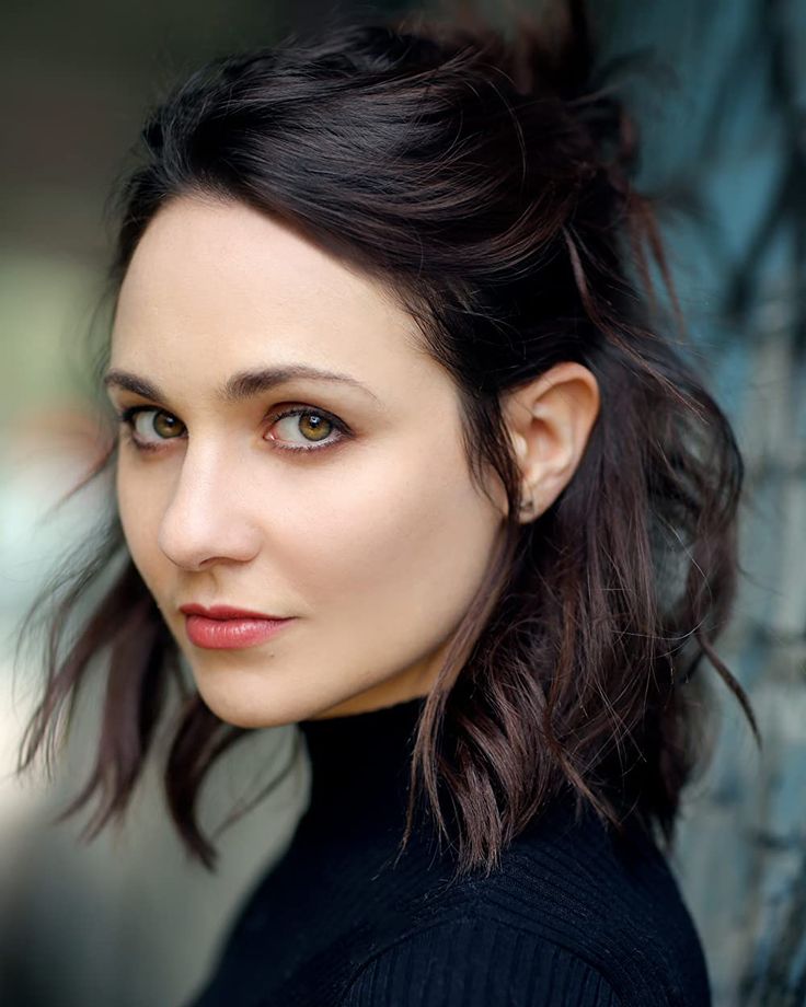 a close up of a person wearing a black shirt and hair in a bun with bangs