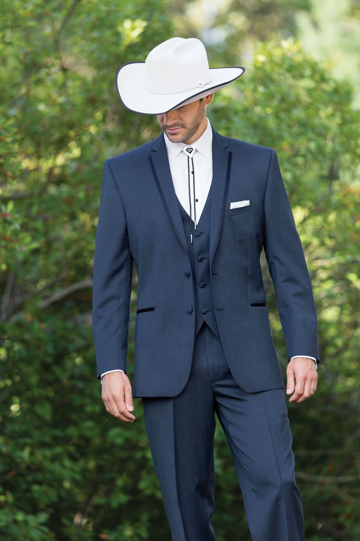 a man in a blue suit and white cowboy hat is standing on the ground with his hands in his pockets