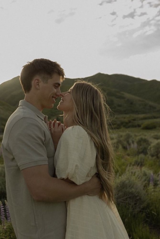 a man and woman standing next to each other in front of a mountain at sunset