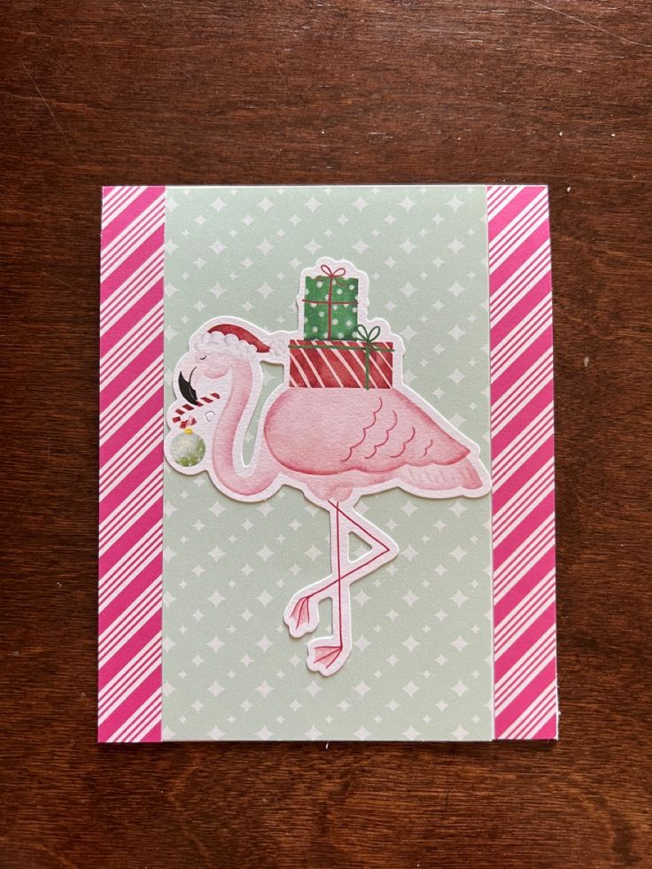 a pink flamingo with a christmas present on it's head sitting on top of a wooden table