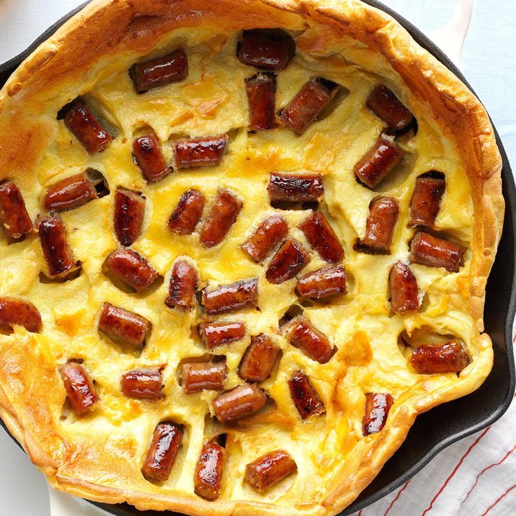 a skillet filled with sausages and cheese on top of a white table cloth