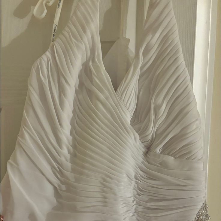 a white wedding dress hanging on a door with some scissors in the background and an empty hanger next to it