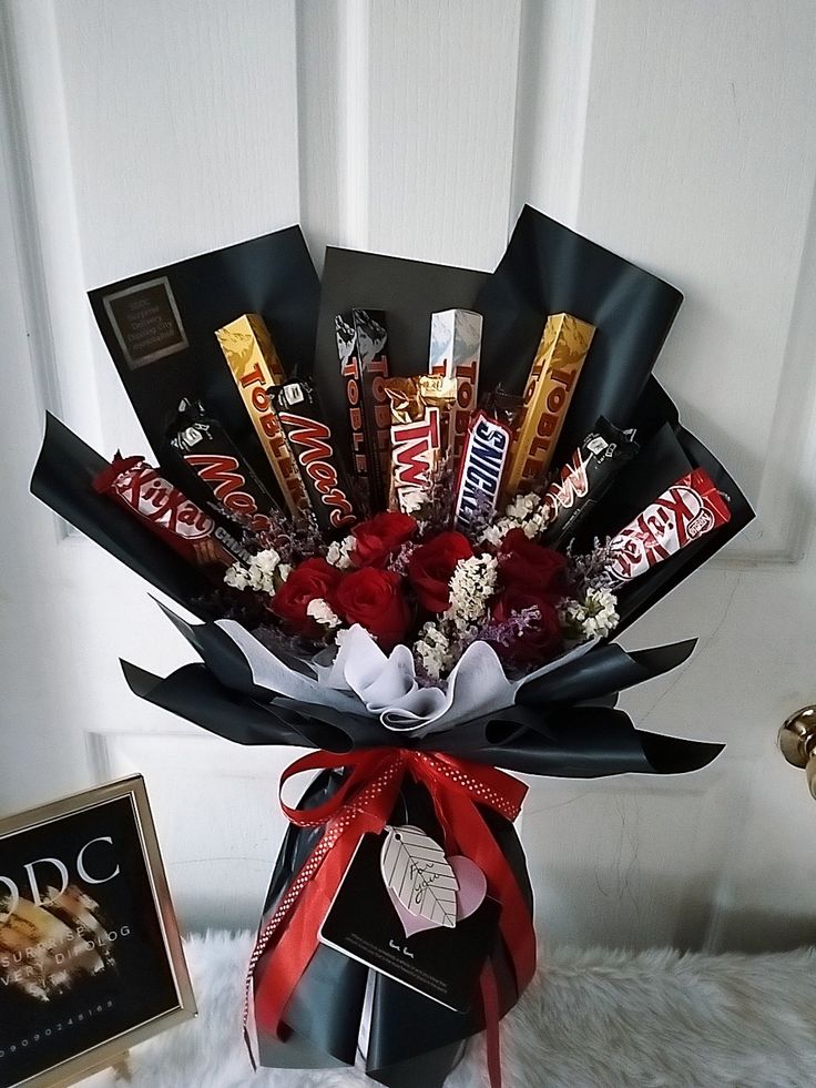 a bouquet of chocolates and candy bars in a gift box next to a framed photograph