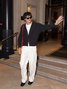 a man in white pants and a black cardigan is standing on some steps with his arms outstretched