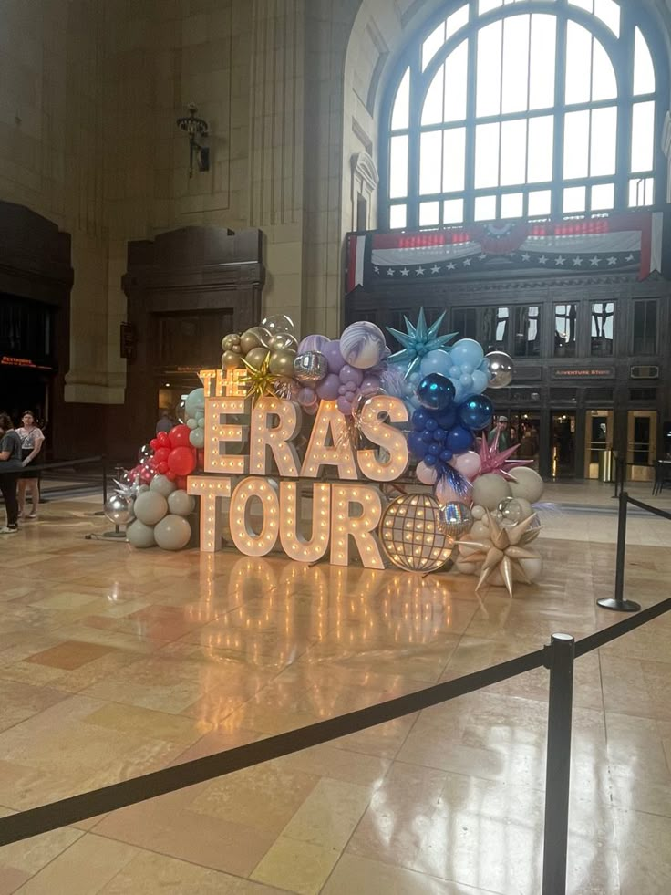 there is a sign that says eras tour in the middle of a room with balloons