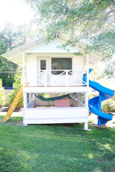 a small white house with a blue slide in the front yard and green grass around it