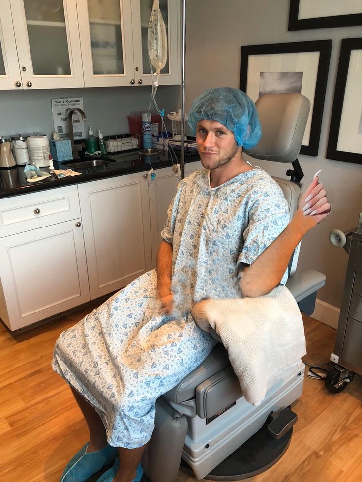 a man sitting in a chair with a blue cap on his head and wearing a surgical gown