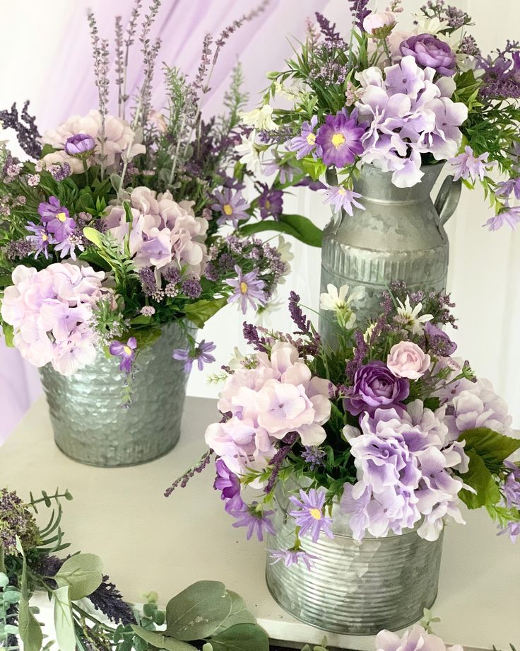 three metal vases filled with purple and white flowers