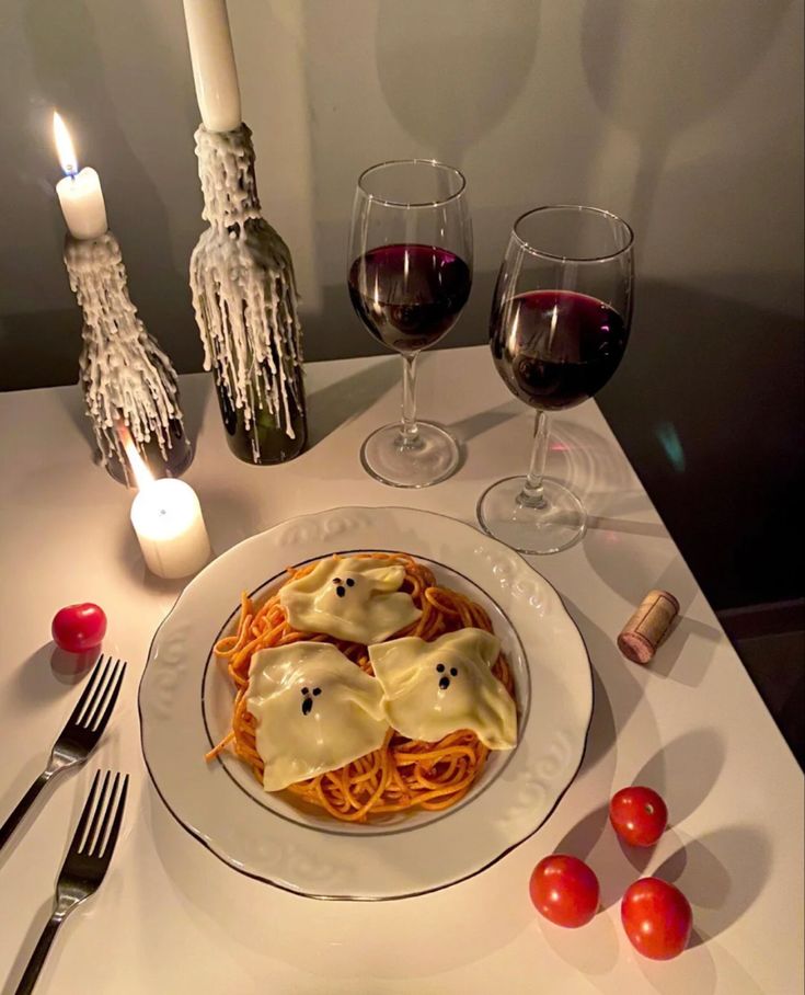 a white plate topped with spaghetti covered in ghost faces next to two glasses of wine