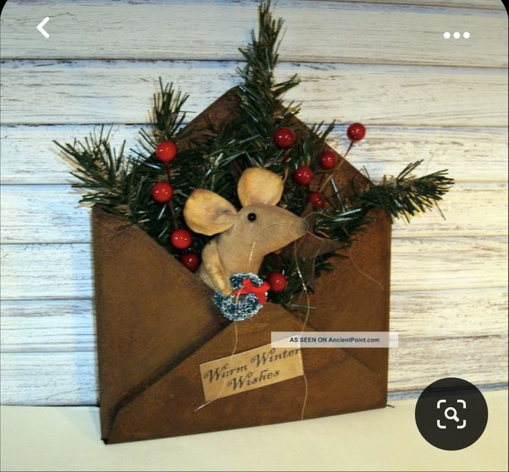 a brown envelope with a mouse in it and some red berries on the top, sitting next to a white wooden wall