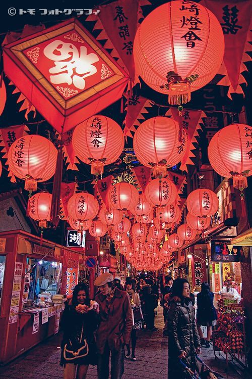 people are walking down the street with lanterns hanging from it's ceiling and in front of them