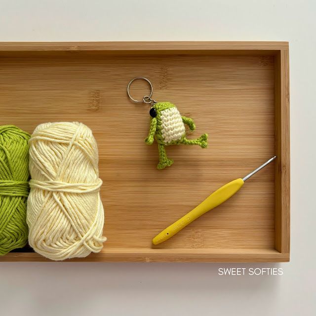 two balls of yarn and a crochet keychain on a wooden tray