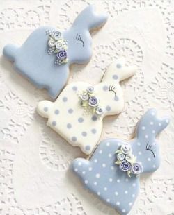 three decorated cookies sitting on top of a white doily covered table with blue and white decorations