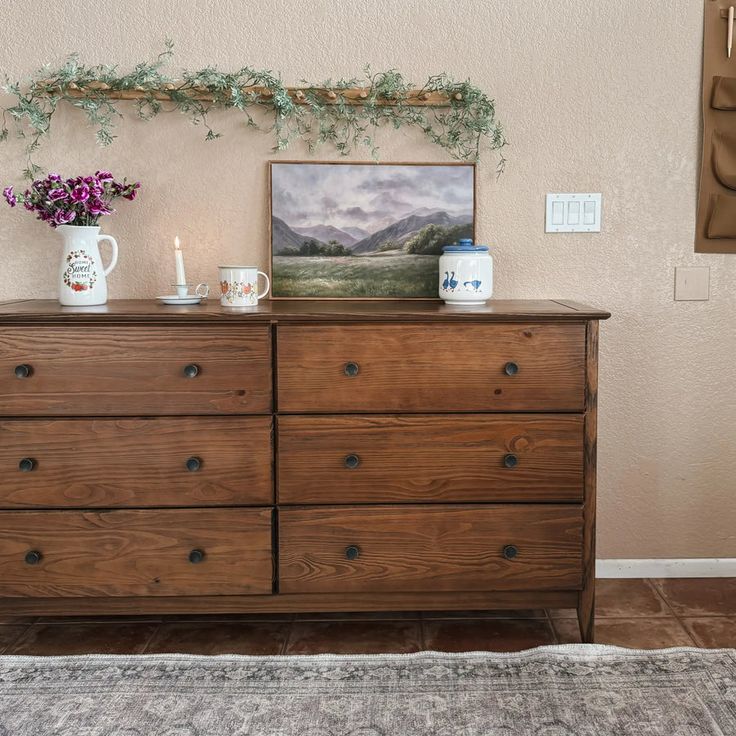 a wooden dresser sitting in front of a painting on the wall