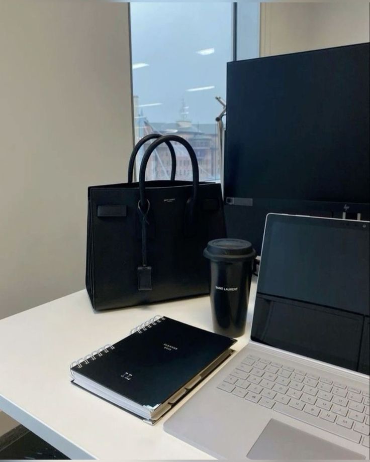 an open laptop computer sitting on top of a white desk next to a black bag