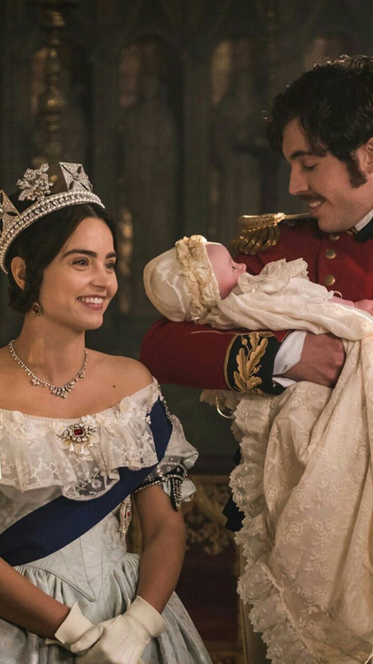 a man holding a baby wearing a tiara next to a woman in a gown