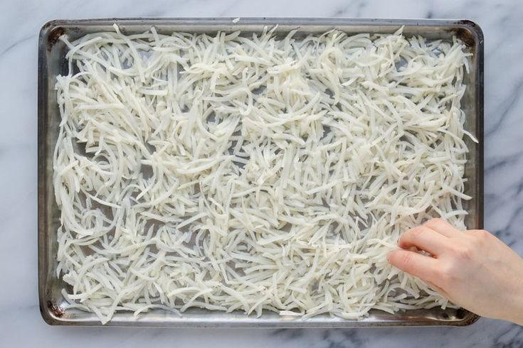 someone is sprinkling shredded white noodles on a baking sheet with a spatula