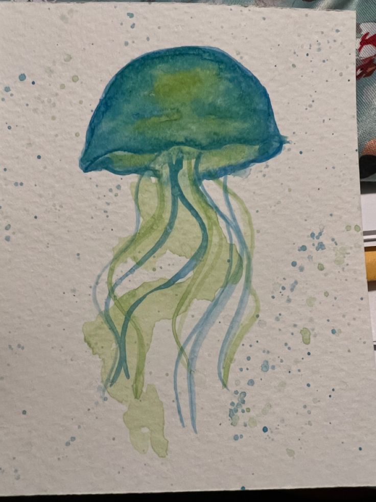 a watercolor painting of a jellyfish in green and blue ink on white paper