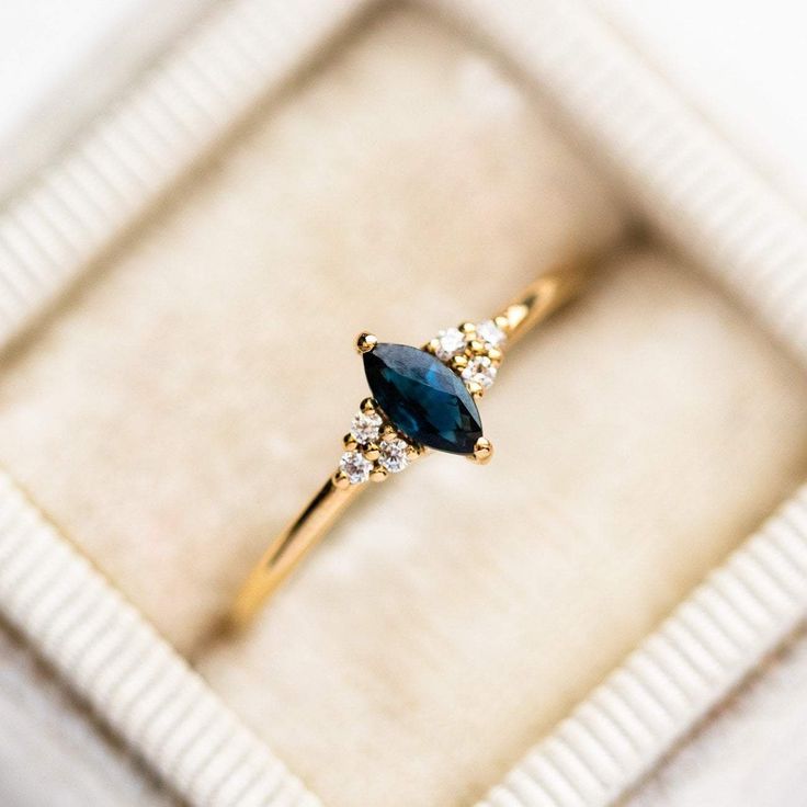 an engagement ring with a blue stone and three diamonds in a white box on top of a table