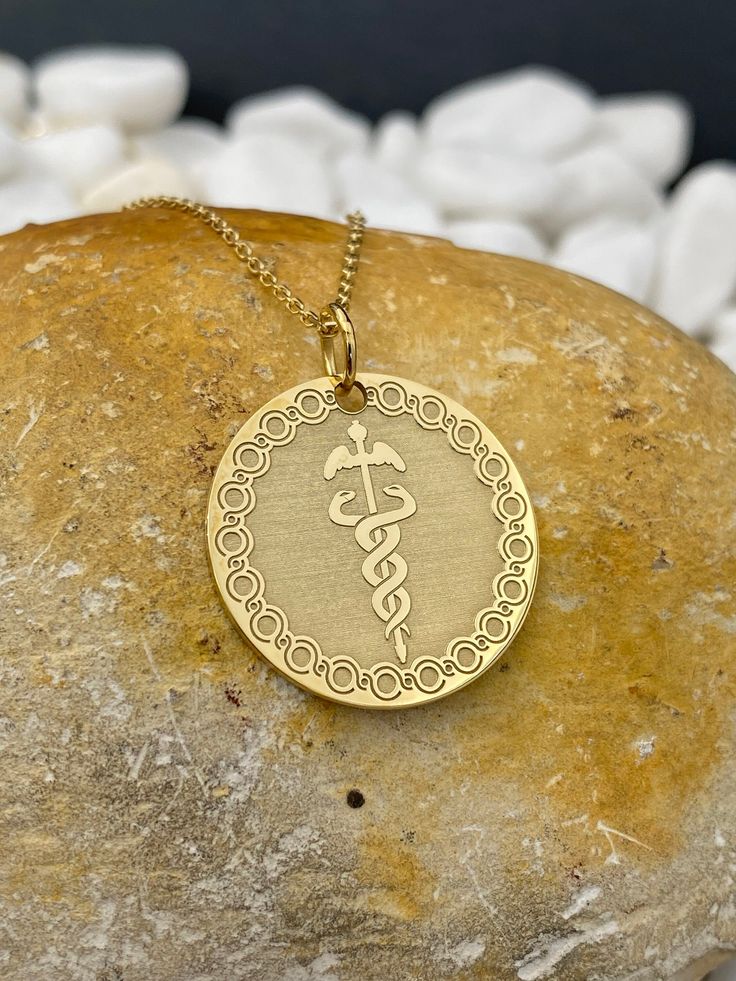 "14k Solid Gold Caduceus Symbol Necklace, Personalized Medical ID Pendant, Medical Alert Pendant, Symbol of Medicine Necklace 14k Solid Gold Choose What Size You Want the Pendant Using The First Option Box Choose Chain Length Or Without Chain Using The Second Option Box Photos Are For The 25.4 mm / 1 Inch Diameter Pendant Pendant thickness : 0.7mm  Contact us if you want it thicker Inner diameter of jump ring : 5mm Contact us if you need it bigger  Chain width : 1.30mm     ♥  Material of pendant and chain: Solid Gold k14  ♥  Packaging: All of our jewelry are beautifully boxed and ready for gifting For more personalized designs take a look here: ♥ www.etsy.com/listing/736955132 ♥ www.etsy.com/listing/819494857 ♥ www.etsy.com/listing/823397880 ♥ www.etsy.com/listing/769847320 ♥ www.etsy.com/ 14k Gold Engraved Medallion Necklace As Gift, Engraved 14k Gold Medallion Necklace Gift, Symbolic 14k Gold Jewelry For Commemoration, Symbolic 14k Jewelry For Commemoration, Symbolic 14k Gold Necklaces Stamped 14k, Symbolic 14k Stamped Yellow Gold Necklace, Symbolic Yellow Gold Medallion Necklace Gift, Gift Yellow Gold Medallion Necklace With Polished Finish, 14k Gold Engraved Medallion Pendant Necklace