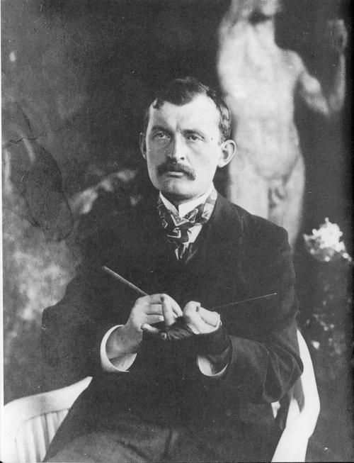 an old black and white photo of a man holding something in his right hand while sitting down