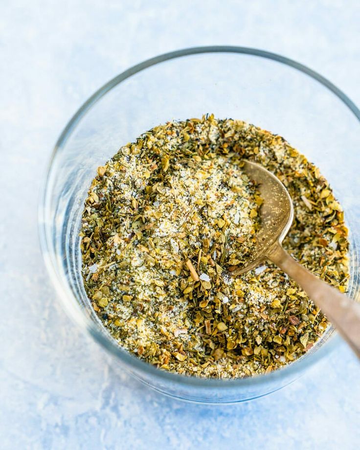 a glass bowl filled with spices on top of a blue countertop next to a wooden spoon