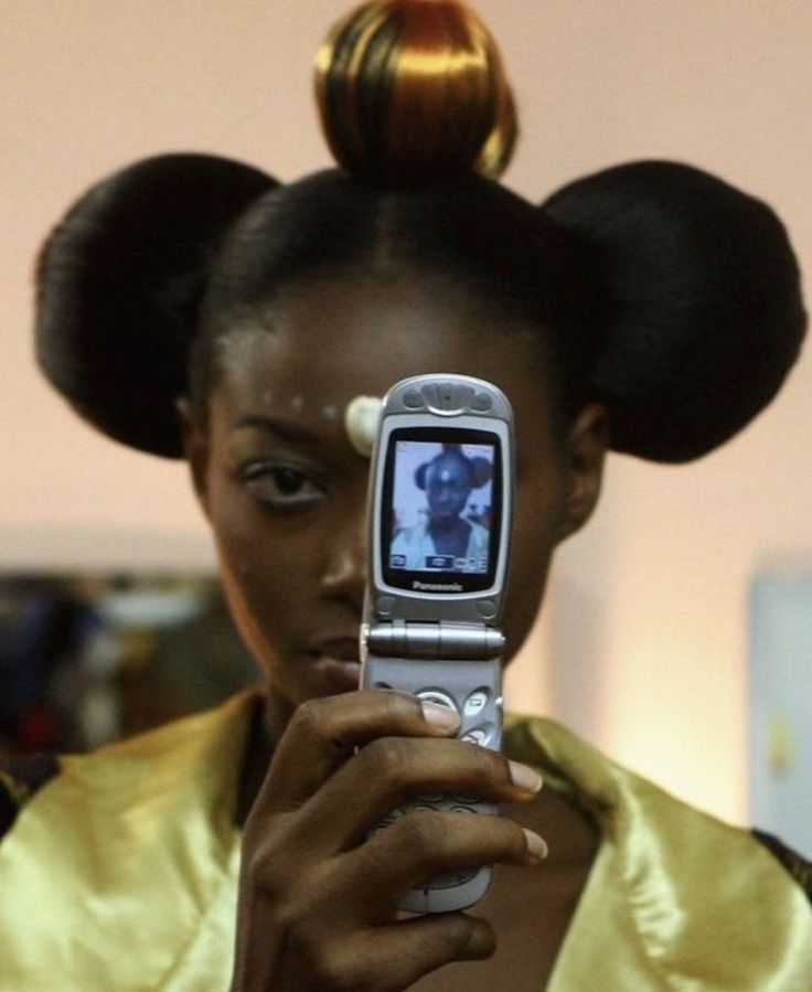 a woman holding a cell phone in front of her face with two buns on top of her head