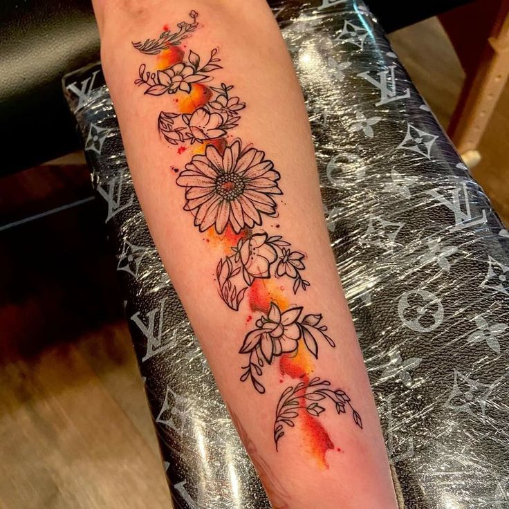 a woman's arm with flowers on it and watercolor paint splatters