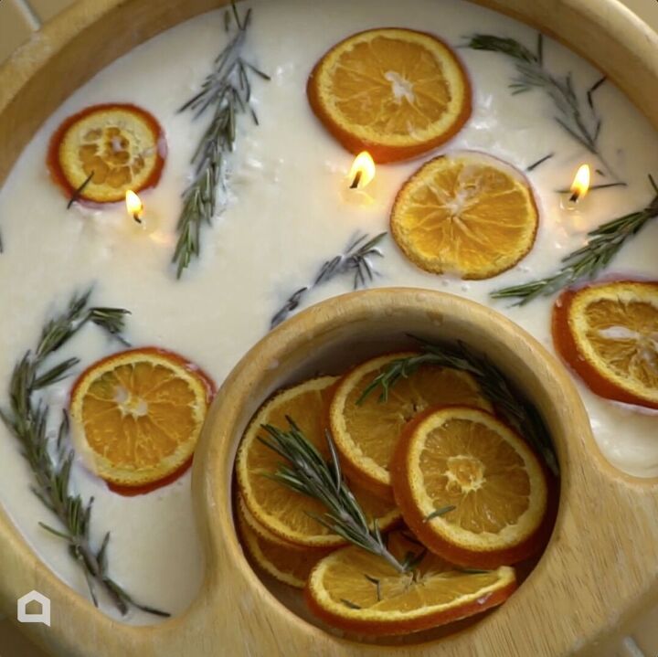 some oranges are in a bowl with rosemary sprigs and candles on the side